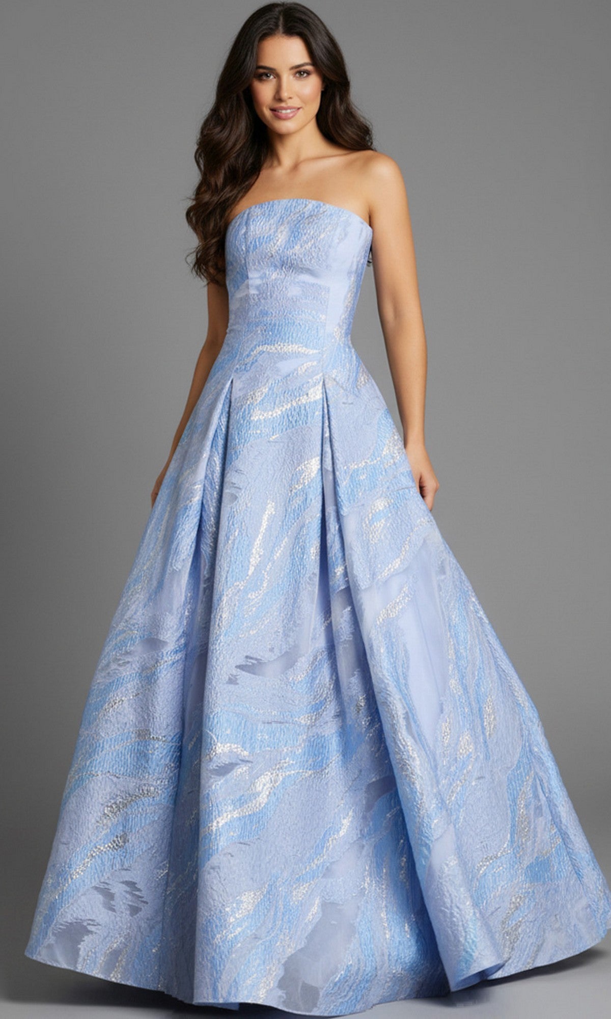 A woman wears the Jovani 44369 long prom dress—a strapless, floor-length jacquard ball gown in light blue with a fitted bodice, flared skirt, and subtle silver pattern.